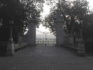Czarno białe zdjęcie przedstawiające kamienną bramę na tle drzew. 