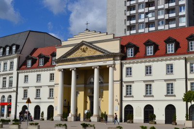 Kolorowe zdjęcie współczesne. Przedstawia widok na kamienice w fasadę kościoła. Jest to kościół  p.w. św. Brata Alberta i św. Andrzeja Apostoła w Warszawie. To tam znajduje się słynny obraz Matki Bożej, który według tradycji pochodzi z ołtarza polowego królów: Jana Kazimierza, Michała Korybuta Wiśniowieckiego a następnie Jana III Sobieskiego. 