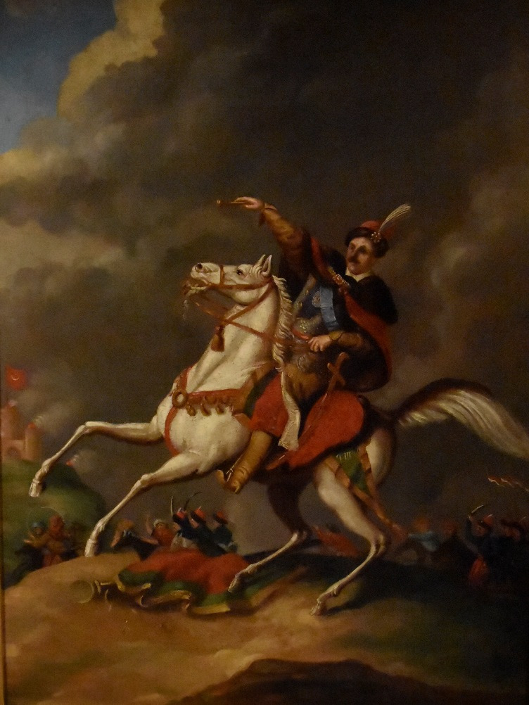 Jan III Sobieski w walce z Turkami. Na pierwszym planie pędzący biały rumak, a na nim Jan III Sobieski ubrany w strój historyczny, który prawą ręką wskazuje gest "Do boju". W tle za nim na drugim planie walczące wojska. Scena rozgrywa się na tle zachmurzonego nieba.