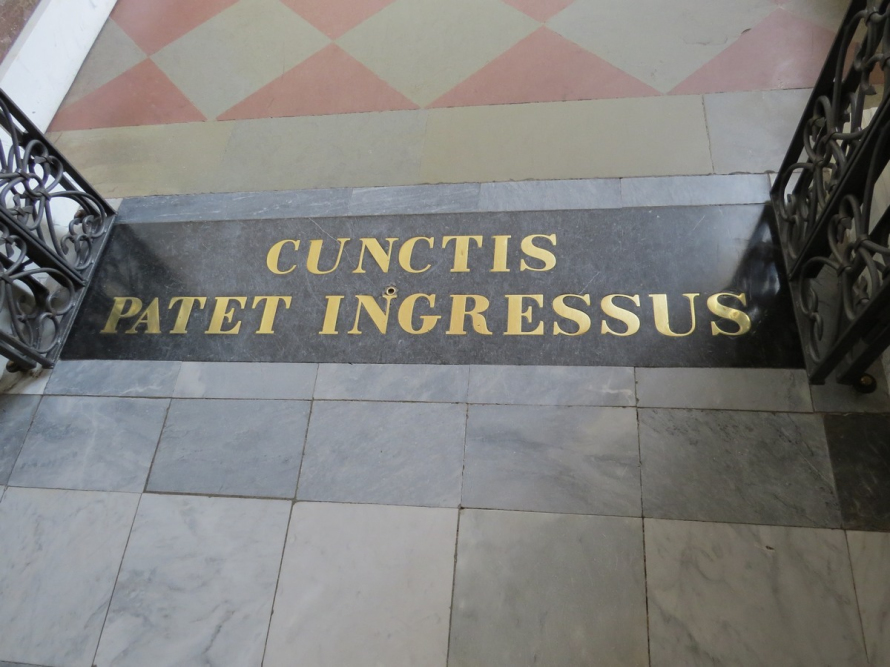 Kolorowe zdjęcie. Przedstawia wejście z marmurową płytą z mosiężnym napisem CUNCTIS PAPTET INGRESSUS (Wszystkim wstęp otwarty).