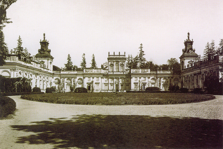 Dawna pocztówka przedstawiająca pałac w Wilanowie. Jest to czarno-biała fotografia, która pokazuje m.in. podjazd do pałacu, fragment zieleni i sam budynek w tle. 