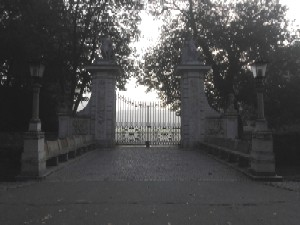 Czarno białe zdjęcie przedstawiające kamienną bramę na tle drzew. 